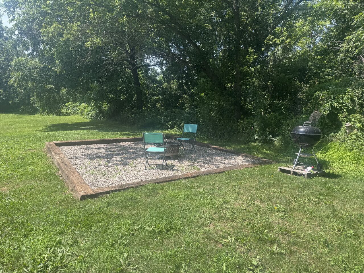 A grassy outdoor area with a fire pit and two chairs.