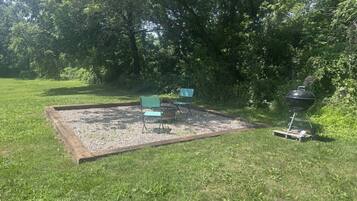 A grassy outdoor area with a fire pit and two chairs.