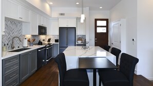 Une cuisine moderne avec des meubles blancs, un réfrigérateur noir et un îlot en marbre agrémenté de chaises noires.