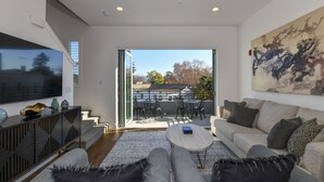 Un salon moderne avec un canapé, une table basse et un téléviseur à écran plat. Il y a un balcon avec du mobilier d’extérieur et une vue sur le paysage.