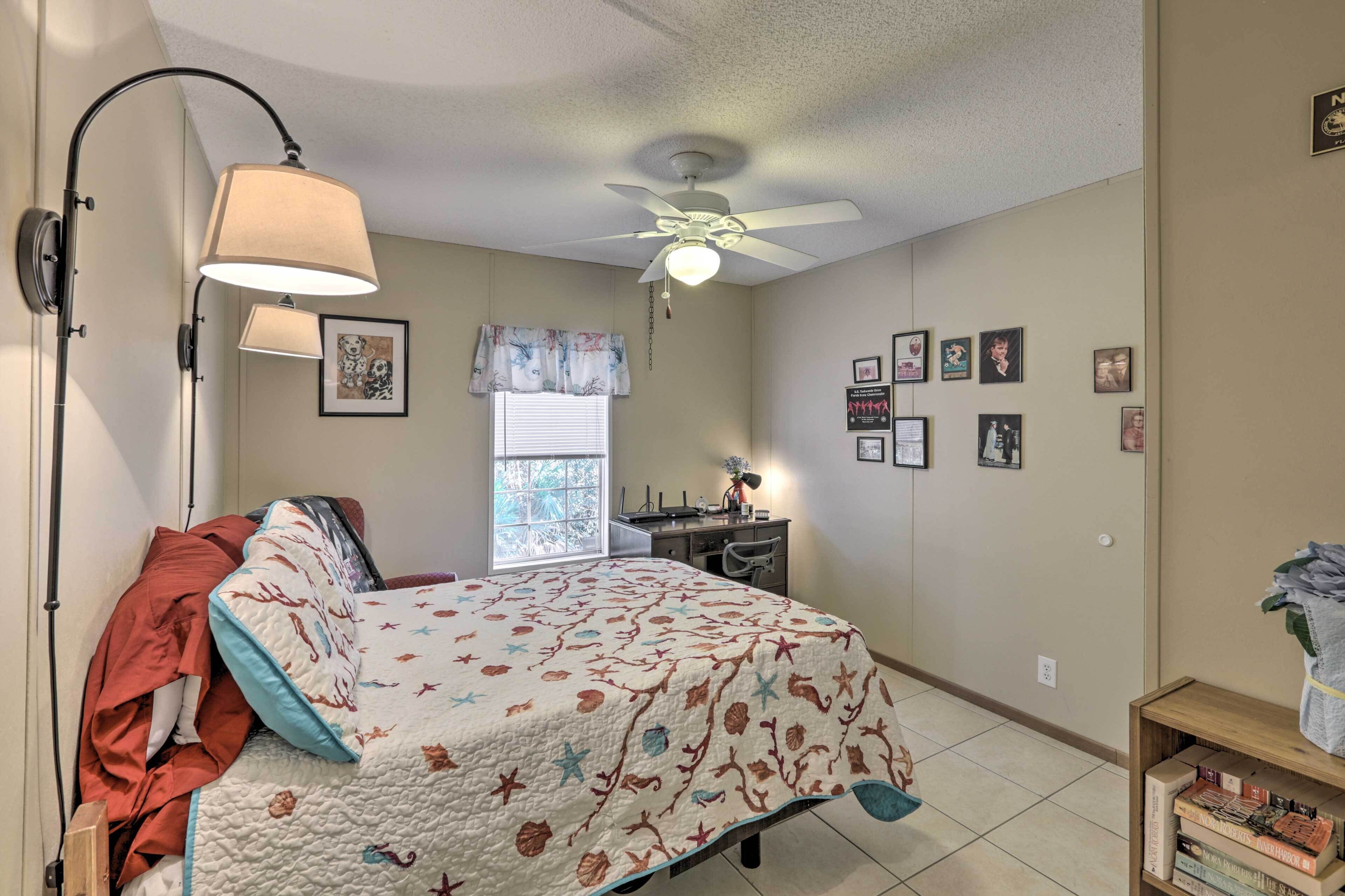 A bedroom with a bed, a desk, a chair, a ceiling fan, and a window with blinds.