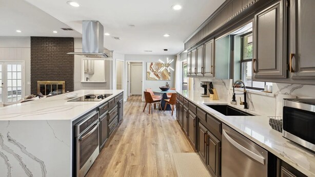A modern kitchen with a central island, stainless steel appliances, and a brick accent wall. - Zen Back Yard with Hot Tub & Firepit: Spa at Home (Dallas)