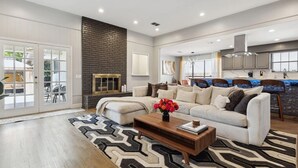 A modern living room with a fireplace, a sofa, a coffee table, and a rug. - Zen Back Yard with Hot Tub & Firepit: Spa at Home (Dallas)