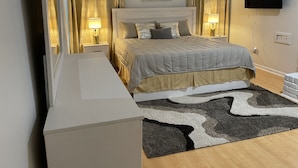 Een slaapkamer met een bed, nachtlampjes, een televisie, een schilderij en een vloerkleed.