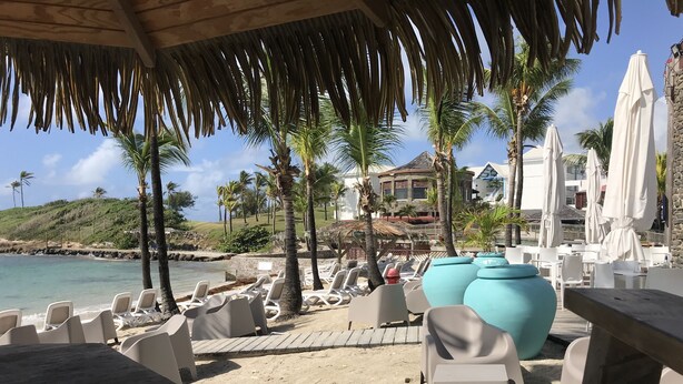 Un espace de détente aménagé sur la plage, avec des chaises longues, une table en bois et des parasols.