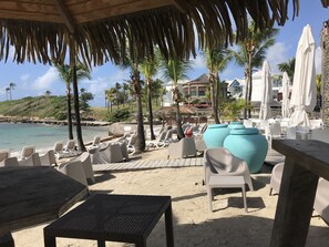 A beachside lounge area with lounge chairs, a wooden table, and umbrellas. - Le CAMASSIA, Luxury Studio in a Private Residence with a Pool and Beach (Saint François)