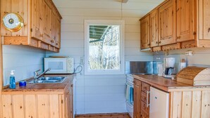 A compact kitchen with wooden cabinets, a microwave, a coffee maker, and a window with a view of trees. - Beach front home in Nordtveitgrend with WiFi (Nordtveitgrend)