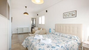 Een slaapkamer met een bed, een stoel, een nachtkastje, een lamp en een lijst aan de muur.
