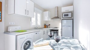 Een moderne keuken met een wasmachine, vaatwasser, magnetron en oven. Er staat een tafel met twee wijnglazen en een boek.