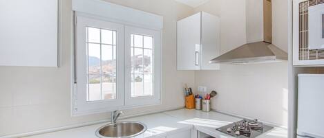 A modern kitchen with white cabinetry, a stainless steel sink, a window with a view of the outside, and a built-in oven.
