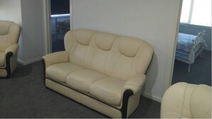 En beige lædersofa i et rum med et stort spejl, der viser en seng og et vindue.