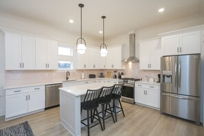 A modern kitchen with white cabinets, stainless steel appliances, and a central island with bar stools. - The Dolly + Iconic Women of Country 4bd Townhome! 8 min ->DT! (Nashville)