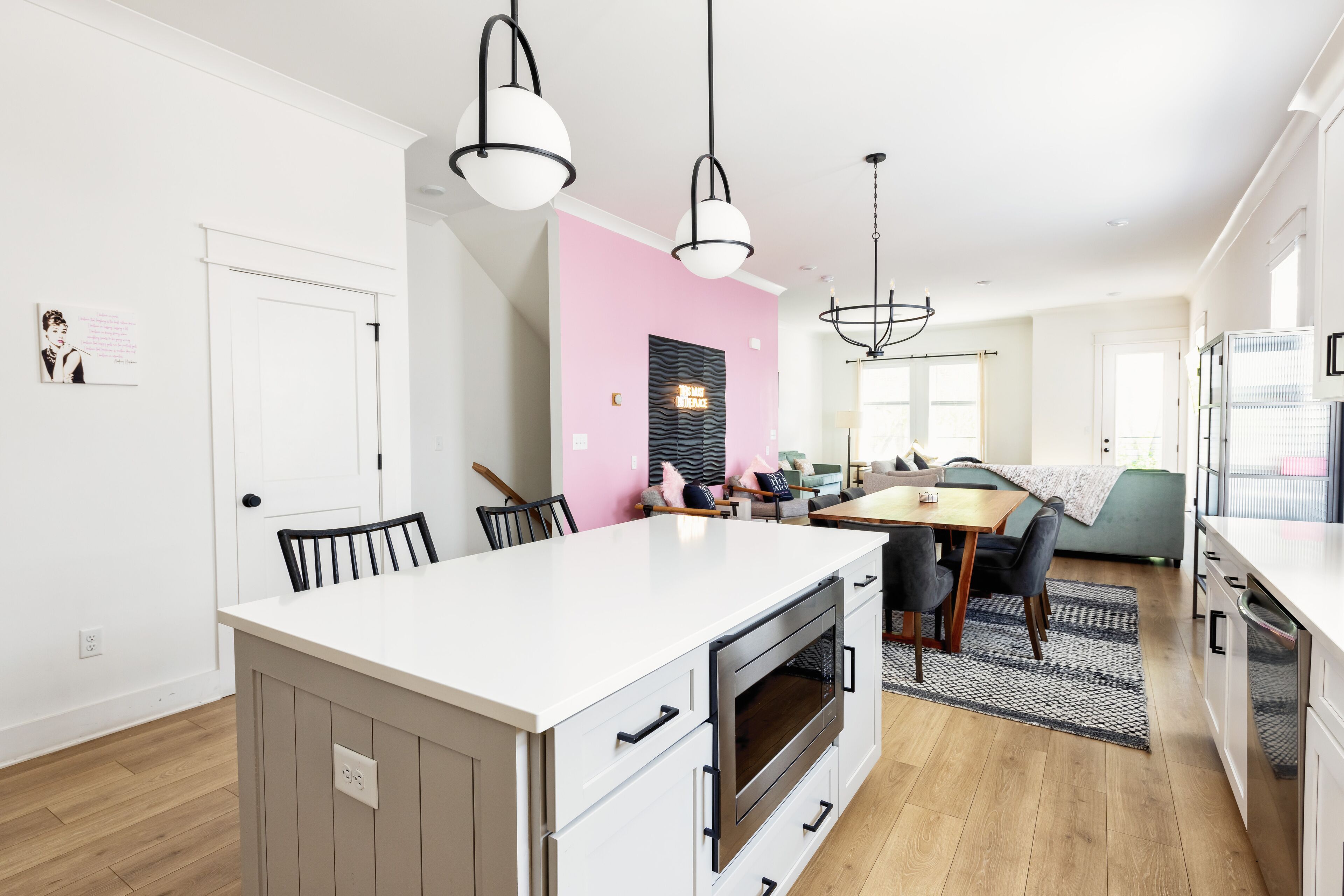 A modern kitchen with a central island, a dining area with a table and chairs, and a pink accent wall.
