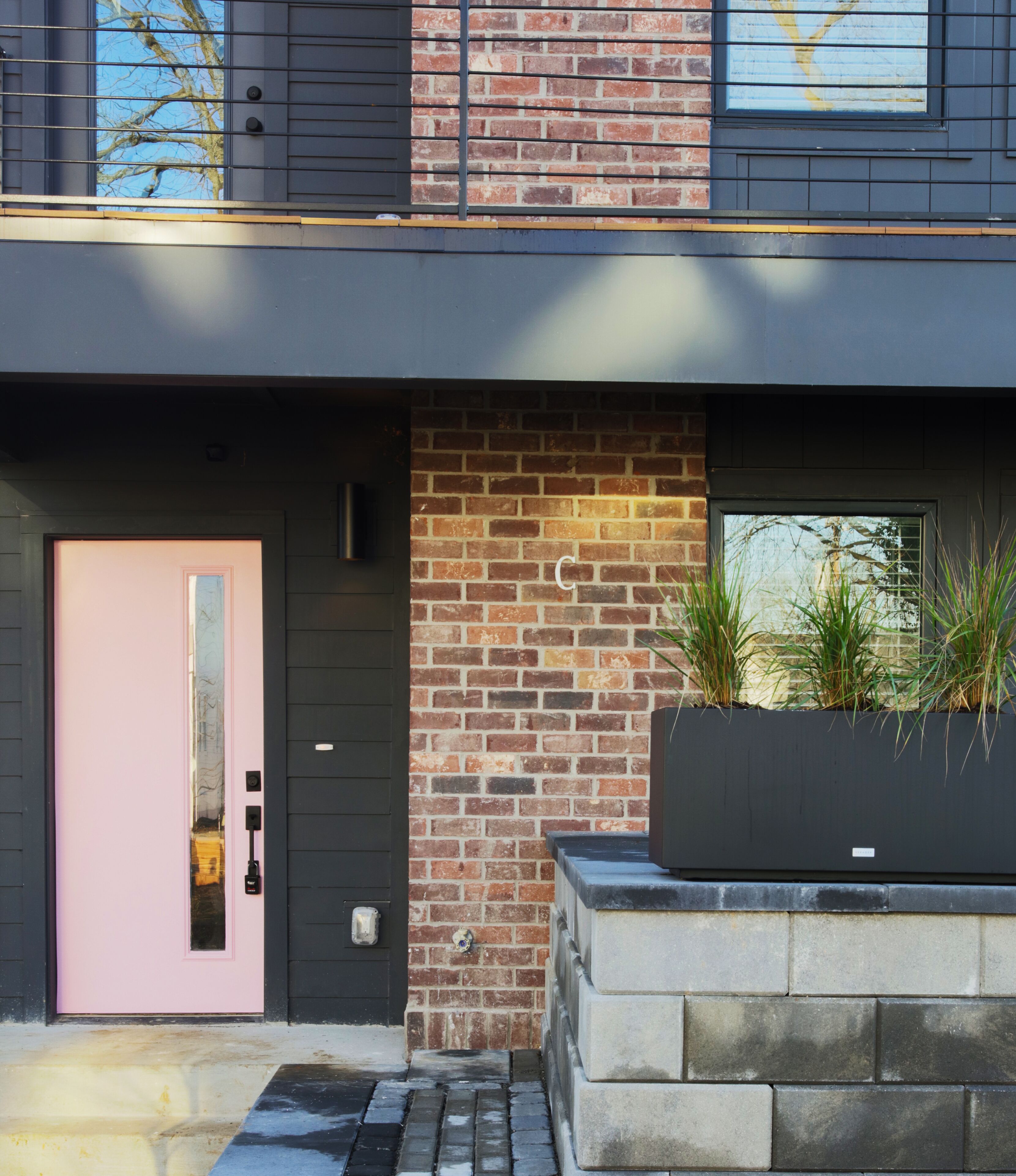 A modern building with a pink door, brick wall, and a planter with plants.