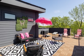 An outdoor patio with a black and white patterned rug, a black metal table, and two pink chairs. - The Dolly + Iconic Women of Country 4bd Townhome! 8 min ->DT! (Nashville)