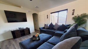 Ein modernes Wohnzimmer mit einer Eckcouch, einem flachbildfernseher an der Wand, einem Couchtisch mit einer Vase und einer Schiebetür zu einem anderen Raum.