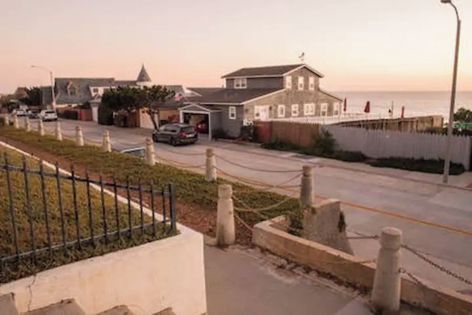 A coastal street with houses, a fence, and a road.