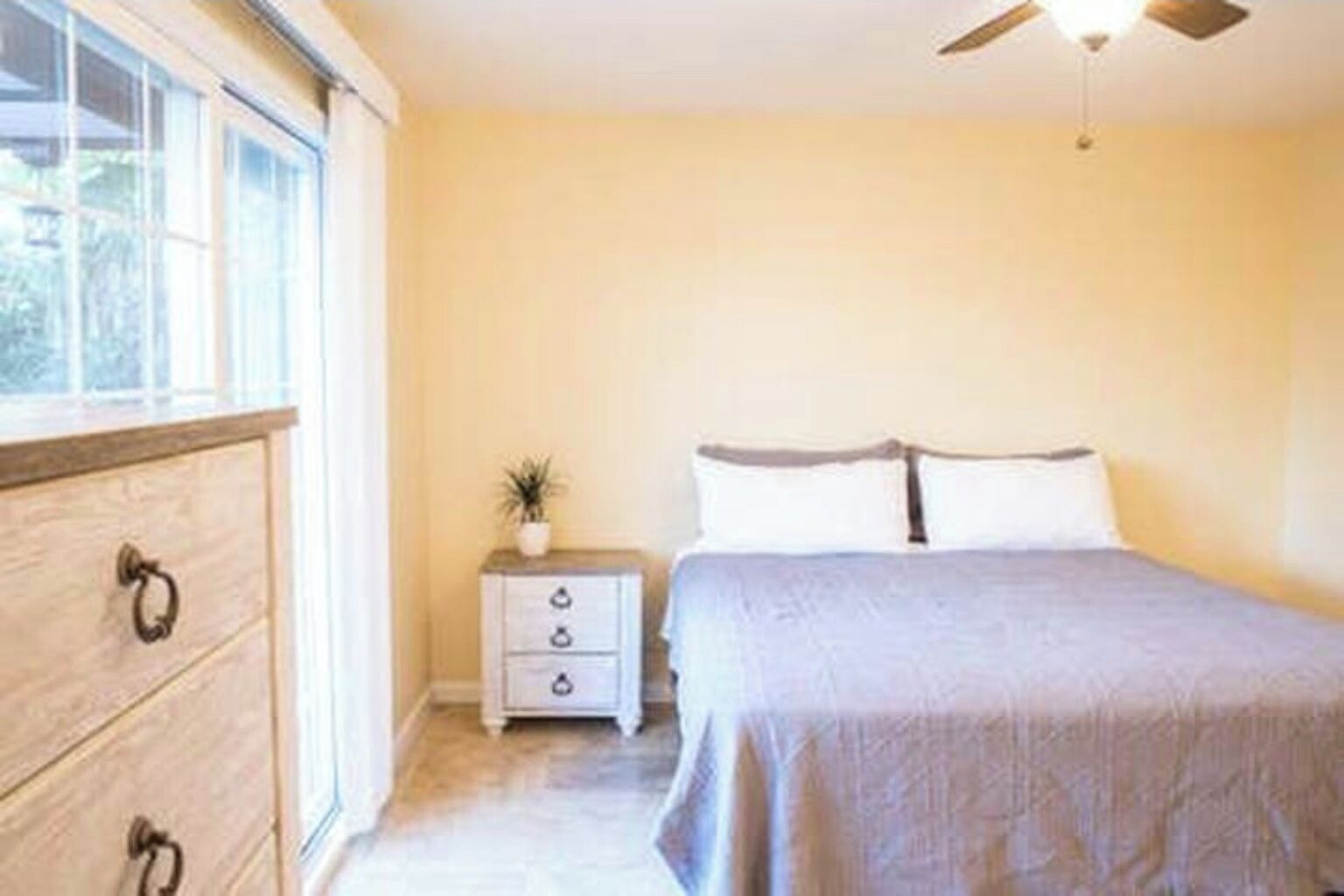 Une chambre à coucher comprenant un lit, une table de chevet, une commode et un ventilateur de plafond.