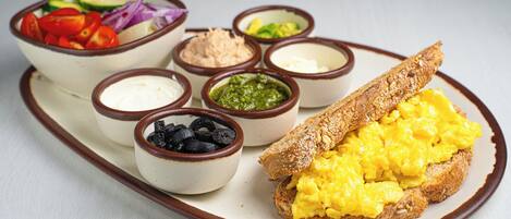 Bandeja de desayuno con huevos revueltos sobre tostadas, ensalada y diferentes salsas.