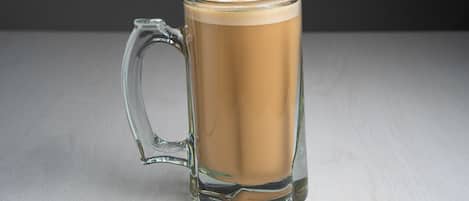 A clear glass mug with a handle, filled with a light brown beverage, placed on a light-colored surface.