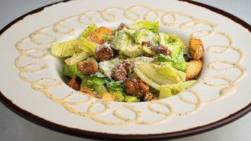 A plate of Caesar salad with croutons and grated cheese, served on a decorative plate with a brown rim.
