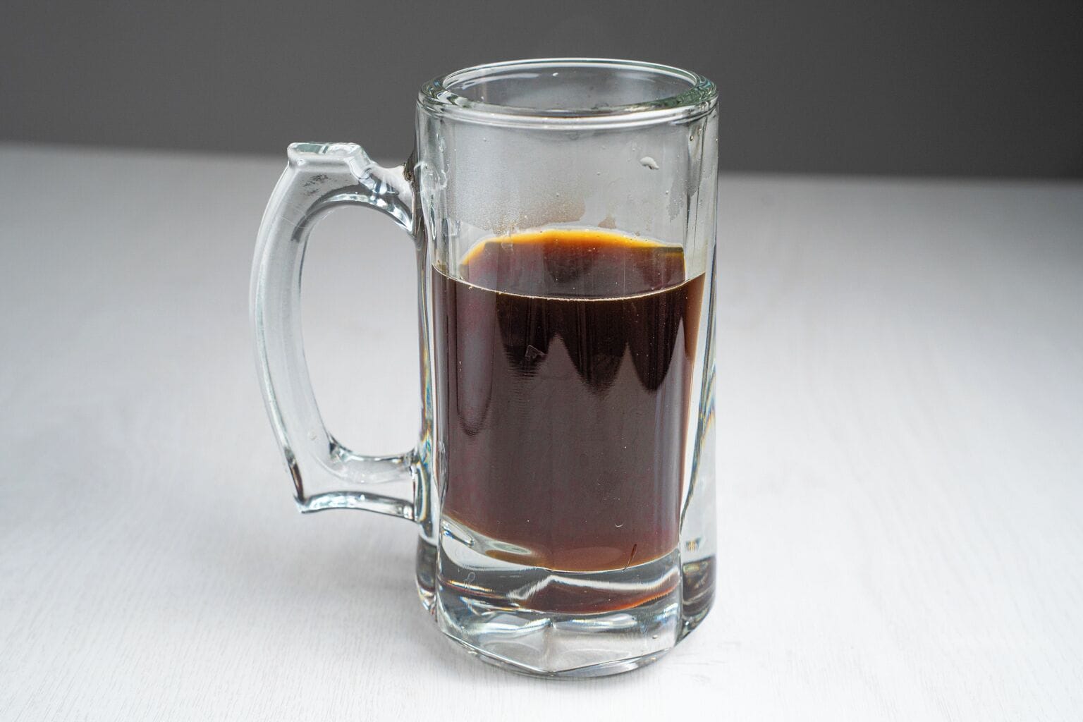 A clear glass mug filled with a dark liquid, likely coffee, on a white surface.
