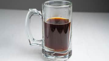 A clear glass mug filled with a dark liquid, likely coffee, on a white surface.