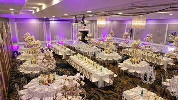 A banquet hall with round tables, white tablecloths, and floral centerpieces.