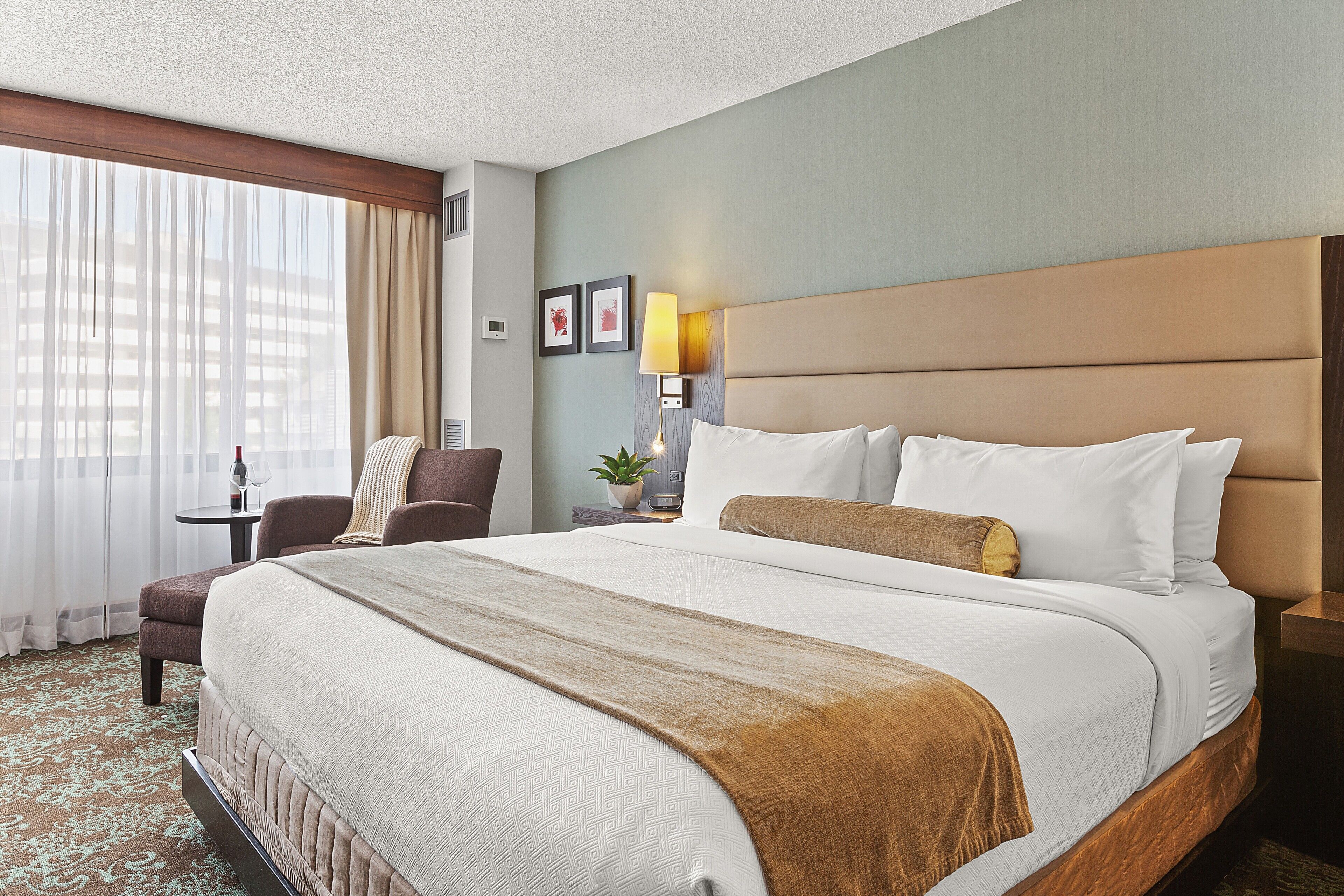 A hotel room with a large bed, a chair, a nightstand, a lamp, and a window with curtains.