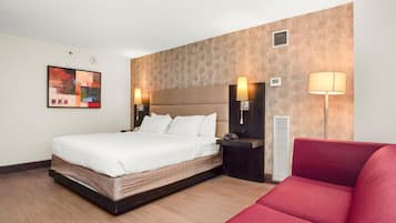 A hotel room with a bed, bedside tables, a red couch, and a wall-mounted artwork.