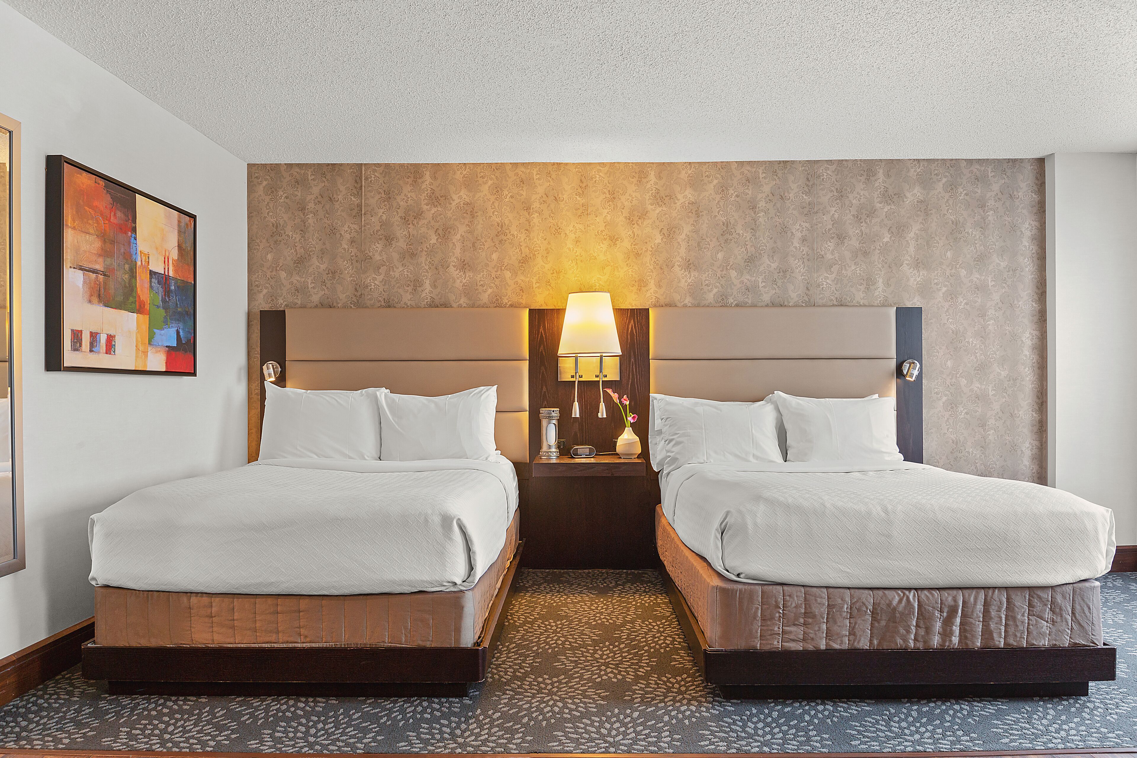A hotel room with two beds, a nightstand with a lamp, and a painting on the wall.