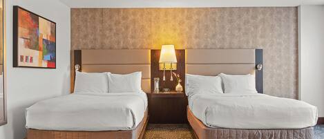 A hotel room with two beds, a nightstand with a lamp, and a painting on the wall.