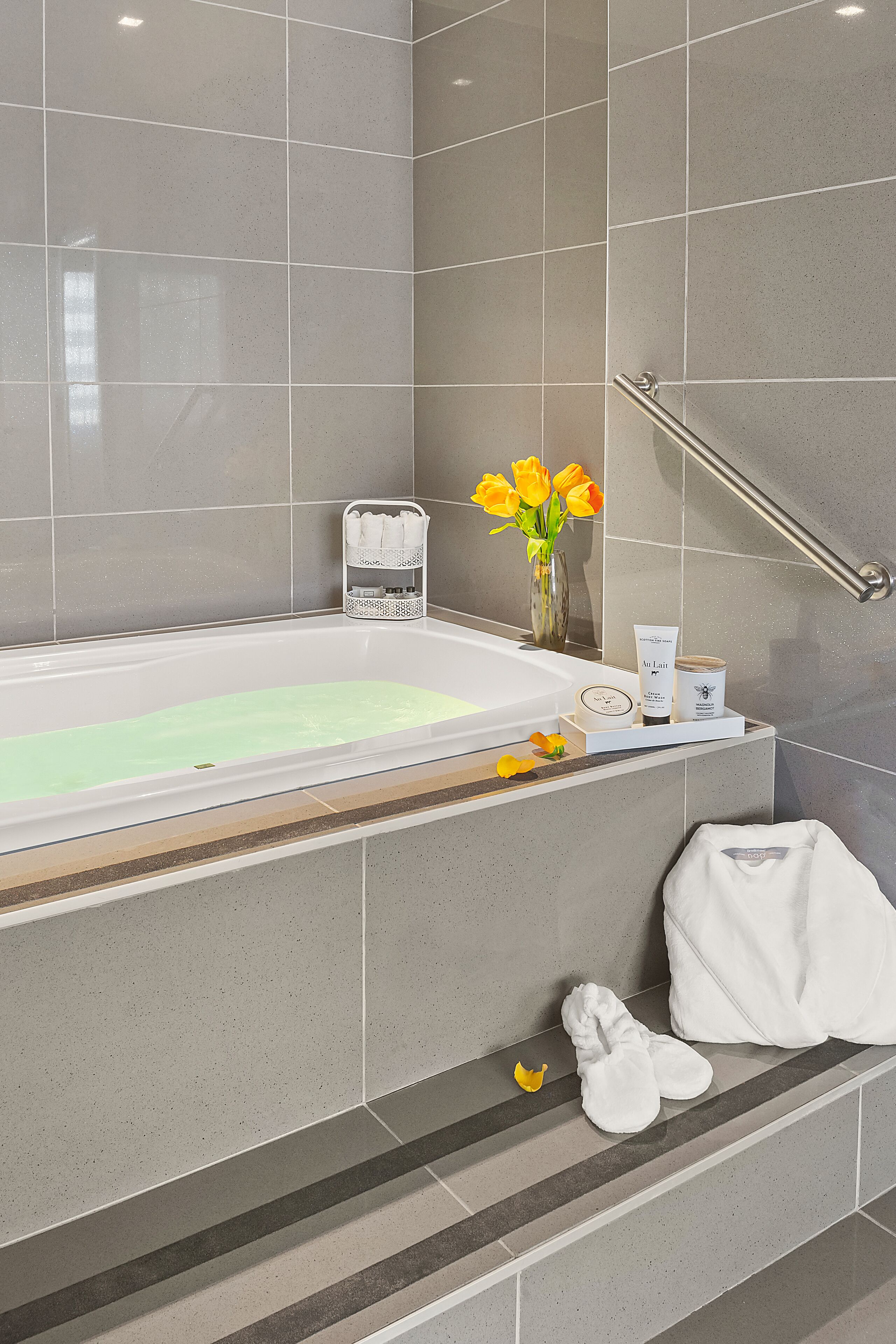 A modern bathroom with a bathtub, a towel rack, and toiletries on a shelf.