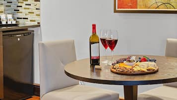 Un coin repas avec une table ronde, deux chaises, une bouteille de vin, deux verres et un plateau de fruits.