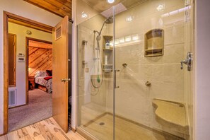 Un cuarto de baño con ducha acristalada, banco incorporado y cabezal de ducha manual.