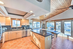 Una cocina moderna con armarios de madera, encimera de granito y una isla grande. Varias ventanas ofrecen vistas del entorno.