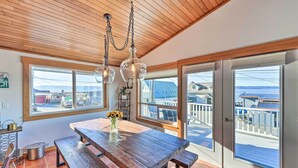 A dining area with a wooden table and benches, large windows with a view of the sea, and a wooden ceiling. - McKees Beach House w/ Ocean Views, Hot Tub! (Stanwood)