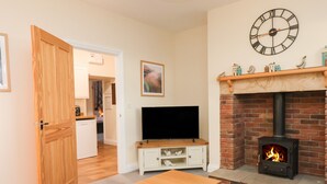 A living room with a TV, a fireplace, and a clock on the wall. - Garden Cottage (Alnwick)