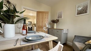 A dining area with a table set for two, a potted plant, a wine bottle, and a wine glass. - Garden Cottage (Alnwick)