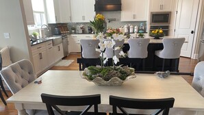 Una cocina moderna con armarios blancos, una isla central con un florero y una mesa de comedor con cuatro sillas.