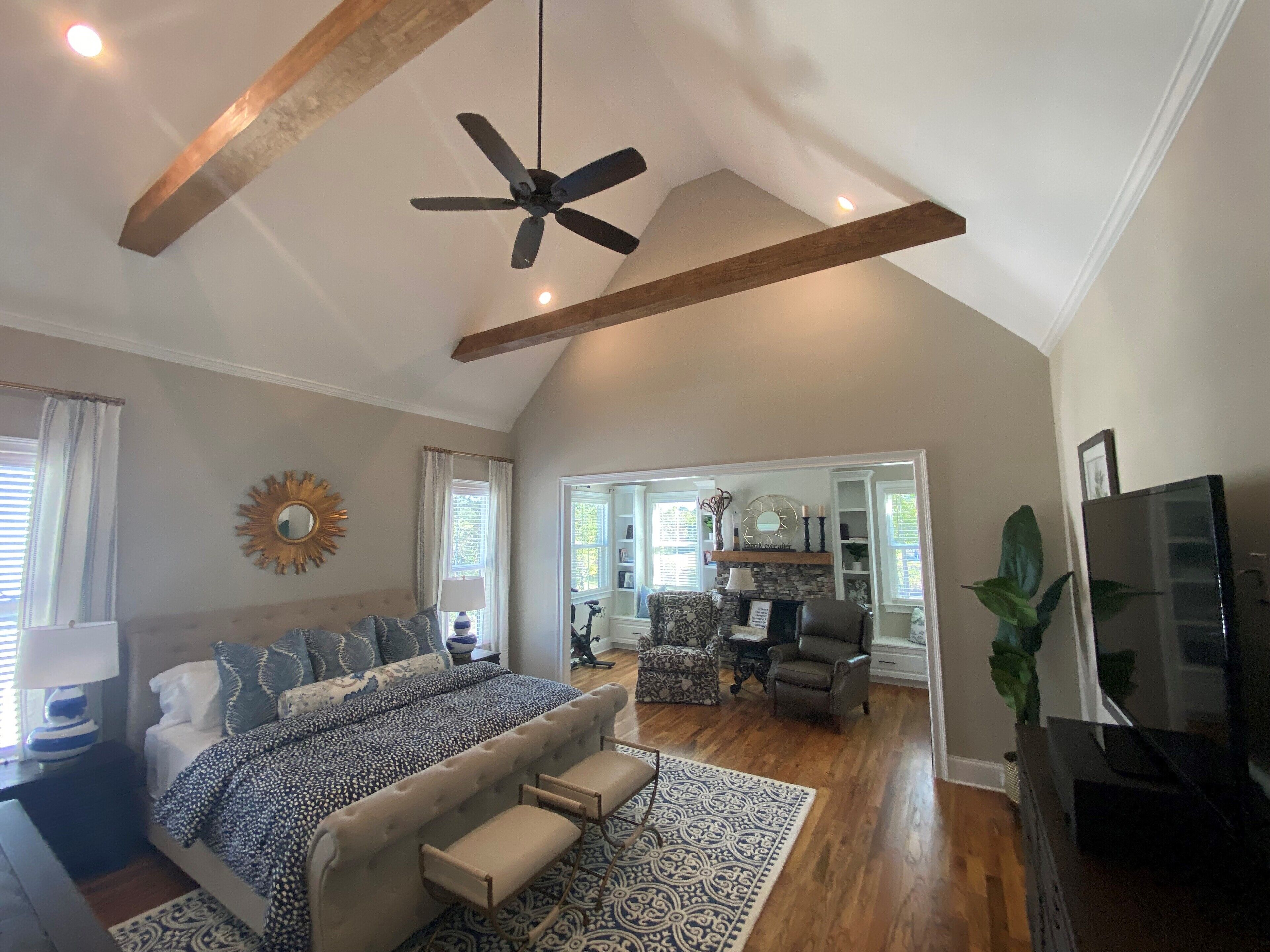 A spacious living room with a high ceiling, a large bed with a patterned bedspread, a ceiling fan, and a television.