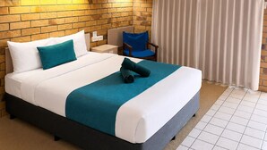 A hotel room with a brick-patterned wall, a bed with white and teal bedding, a ceiling fan, and a window with curtains. - Boulder Opal Motor Inn (Winton)