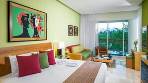 A hotel room with a large bed, a sofa, a chair, a desk, and a balcony with a view of greenery. - Grand Mayan (Playa del Carmen)