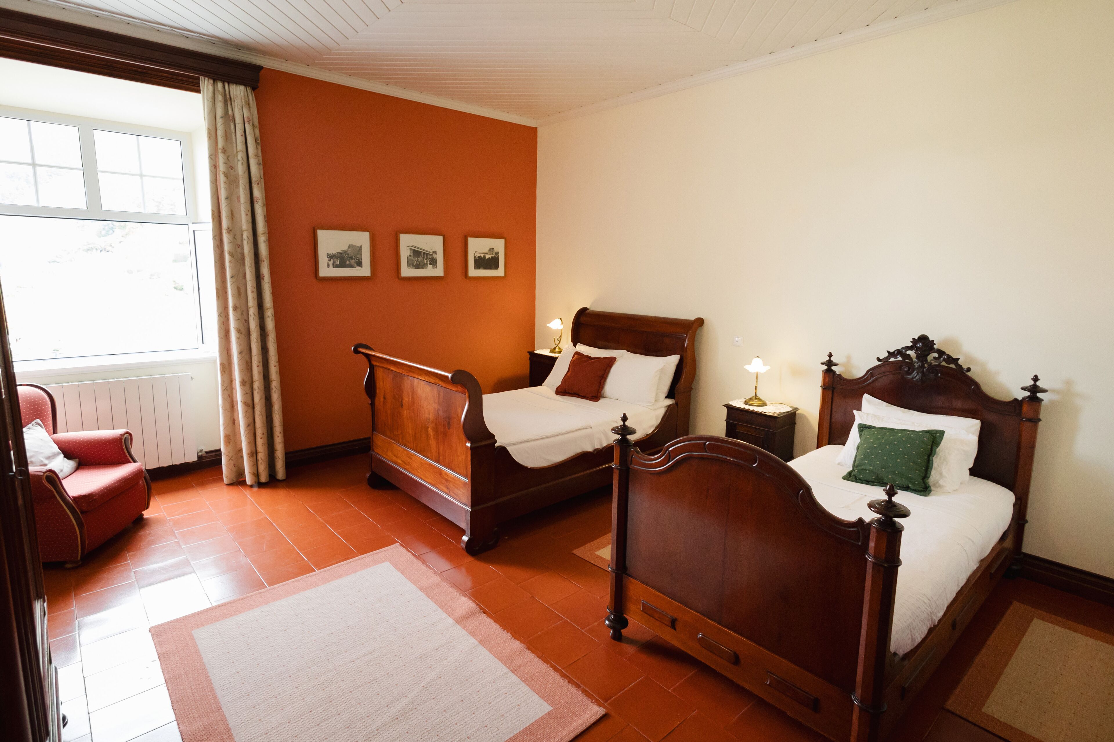Een slaapkamer met twee houten bedden, een rode stoel en een raam met gordijnen.