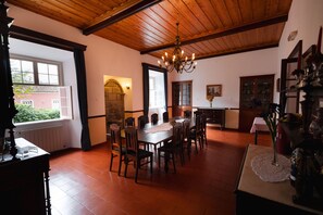 A dining area with a wooden table and chairs, a chandelier, and a view of the outside. - Solar de Lalem (Ribeira Grande)