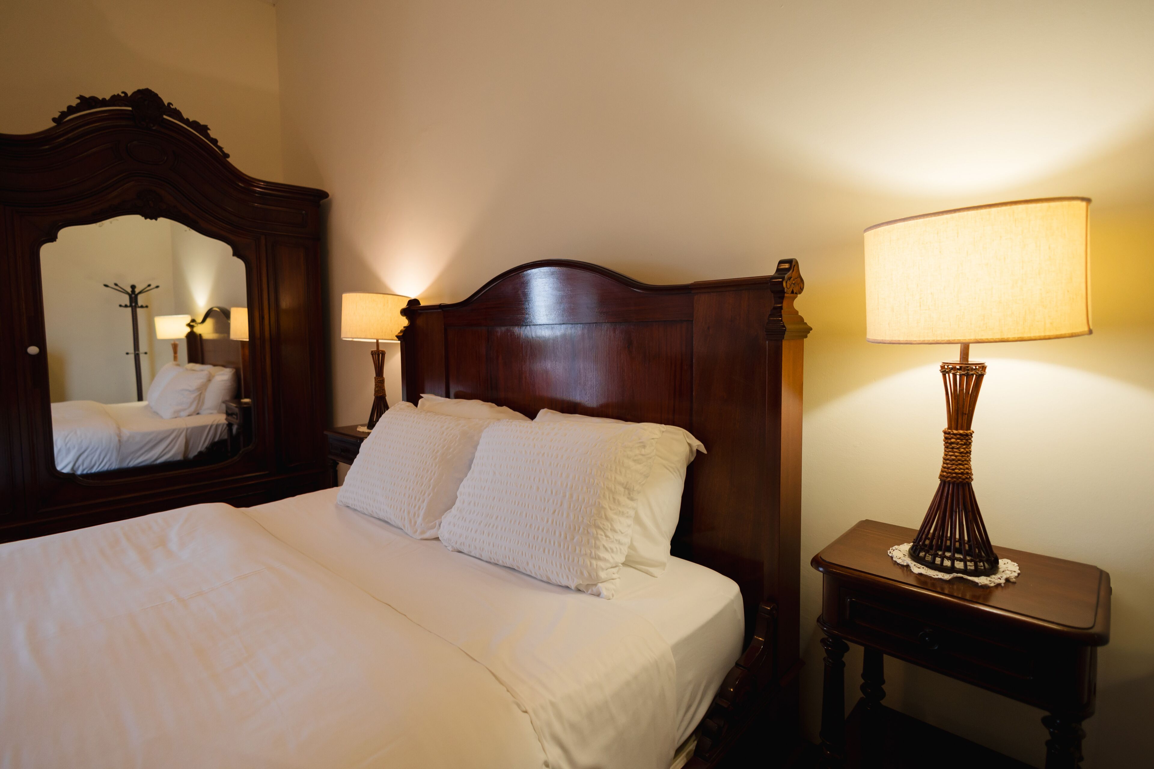 A neatly made bed with white linens, a wooden headboard, and two bedside lamps.
