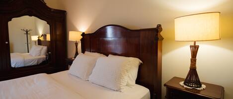 A neatly made bed with white linens, a wooden headboard, and two bedside lamps.