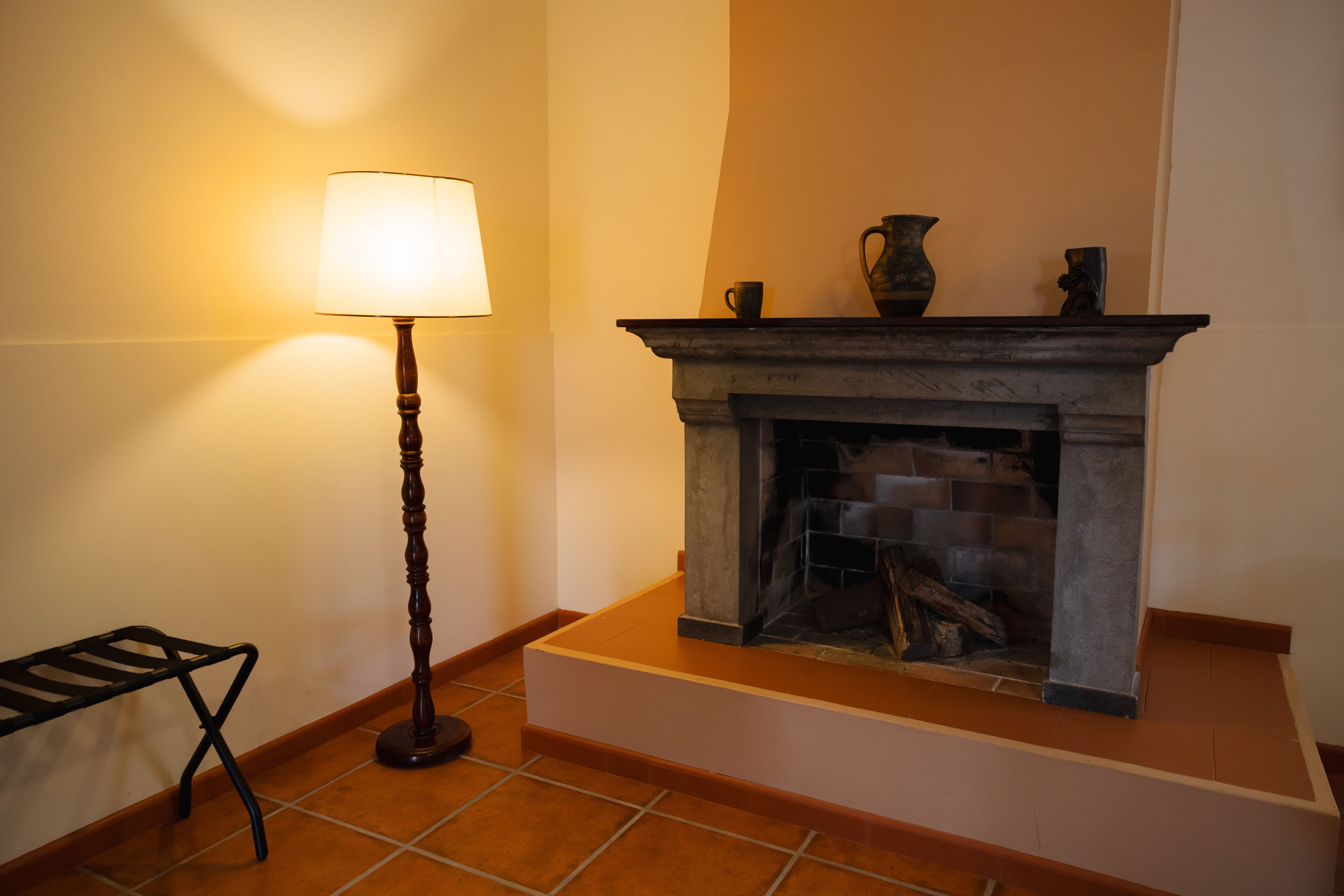 Una chimenea con repisa, una lámpara de pie y una mesita.