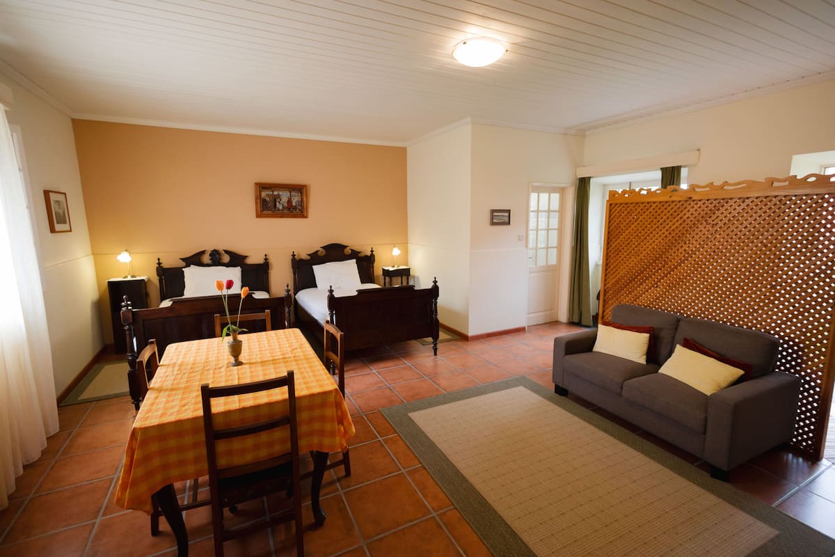 Una habitación con cama, sofá, mesa de comedor con sillas y una mesita de noche con lámpara.