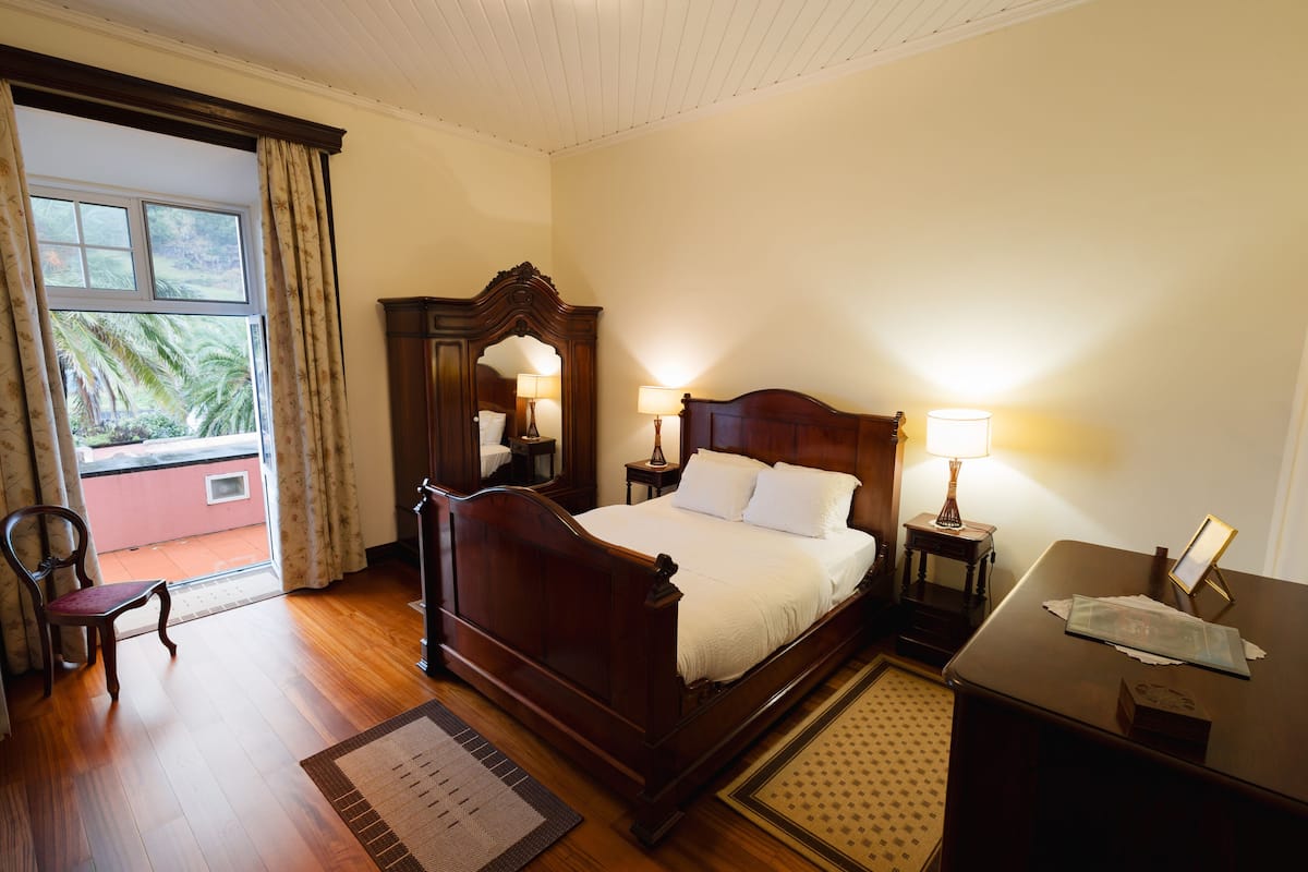 Una habitación de hotel con una cama de madera, dos lámparas de noche, una mesita de noche, un escritorio y una silla.